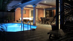 A swimming pool with a wooden deck, lounge chairs, and a covered patio area. - FRONT de MER, Standing Villa, 20 m from the Ocean, swimming pool, Saint-Pierre - (Saint-Pierre)