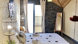 A bedroom with a large bed, a wooden floor, a stone wall, and a balcony with curtains. - FRONT de MER, Standing Villa, 20 m from the Ocean, swimming pool, Saint-Pierre - (Saint-Pierre)