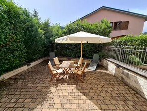 Een terras met een ronde houten tafel, stoelen, een parasol en een vloer van baksteen.