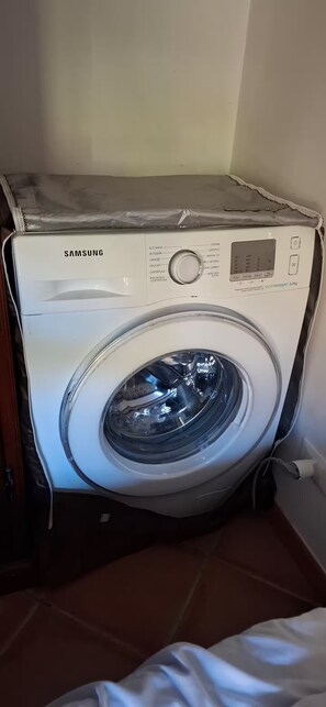 A Samsung washing machine with a control panel, a transparent door, and a power cord plugged in.