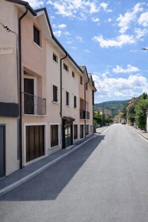 Vista de una calle en zona residencial, con edificios de varios pisos, cielo despejado y colinas al fondo.