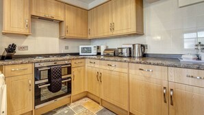 Une cuisine moderne dotée de meubles en bois, d’un four à micro-ondes, d’un grille-pain, d’une bouilloire et d’une cuisinière à gaz.