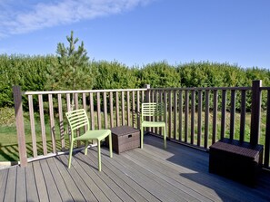 A wooden deck with two green chairs and a small table, surrounded by a wooden railing.