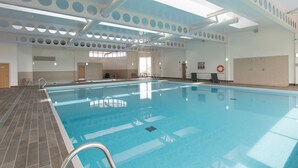 Una piscina interior con suelo de baldosas, escalera metálica y techo con aberturas circulares.