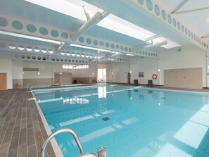 Une piscine intérieure dotée d’un sol carrelé, d’un escalier métallique et d’un plafond orné d’ouvertures circulaires.