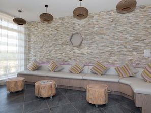 Un intérieur moderne avec un mur en pierre, un banc rembourré agrémenté de coussins à rayures et des tabourets en bois.