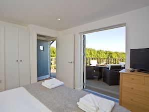 Ein Schlafzimmer mit Bett, Schminktisch, Fernseher und einem Balkon mit Gartenmöbeln.
