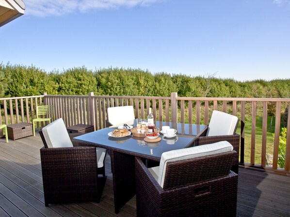 Une terrasse avec une table dressée pour le petit-déjeuner, des chaises en osier et une vue sur un paysage verdoyant.