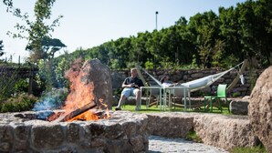 A stone fire pit with flames, a hammock, and a person sitting on a chair.