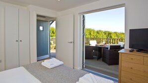 Un dormitorio con cama, cómoda, televisor y balcón con mobiliario exterior.