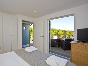 Une chambre à coucher comprenant un lit, une commode, un téléviseur et un balcon aménagé avec du mobilier d’extérieur.