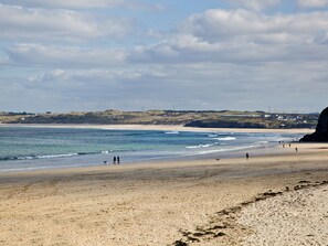 Une plage avec un rivage sablonneux, un ciel dégagé et des collines à l’horizon.