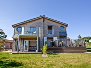 Une maison à deux étages avec une terrasse, de grandes fenêtres et un petit jardin.