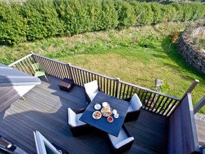 Une terrasse dotée de mobilier d’extérieur, d’une table dressée pour un repas et offrant une vue sur la verdure environnante.