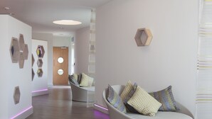 Un interior moderno con un sofá blanco curvo, decoraciones murales hexagonales y una puerta de madera.