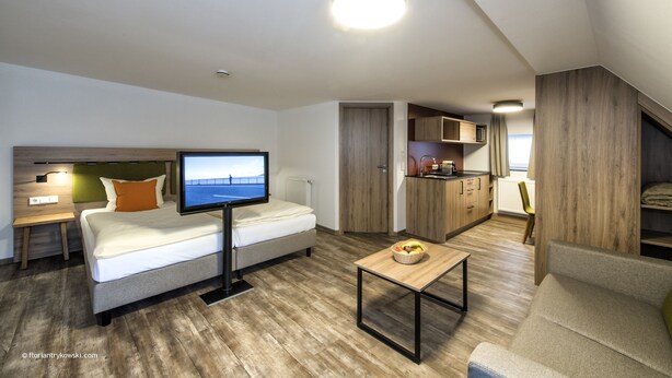 A modern, compact living space with a bed, a television, a small table, and a kitchenette. - Übernachten in der Tenne (Nuremberg)