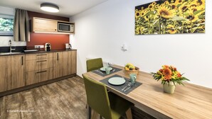 A modern kitchen with wooden cabinets, a microwave, and a dining area with a table set for two. - Übernachten in der Tenne (Nuremberg)