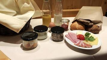 A breakfast table with bread, cheese, ham, tomatoes, and condiments.