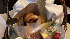 A wicker basket containing bread, a jar of milk, a bottle of juice, a plate with cheese, ham, tomatoes, and a boiled egg. - Übernachten in der Tenne (Nuremberg)