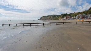 Ein Strand mit einer Holzbarriere, ruhiger See und Gebäuden an einem Hügelhang.