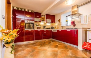 Uma cozinha com armários vermelhos, piso ladrilhado e diversos eletrodomésticos, incluindo micro-ondas e forno.