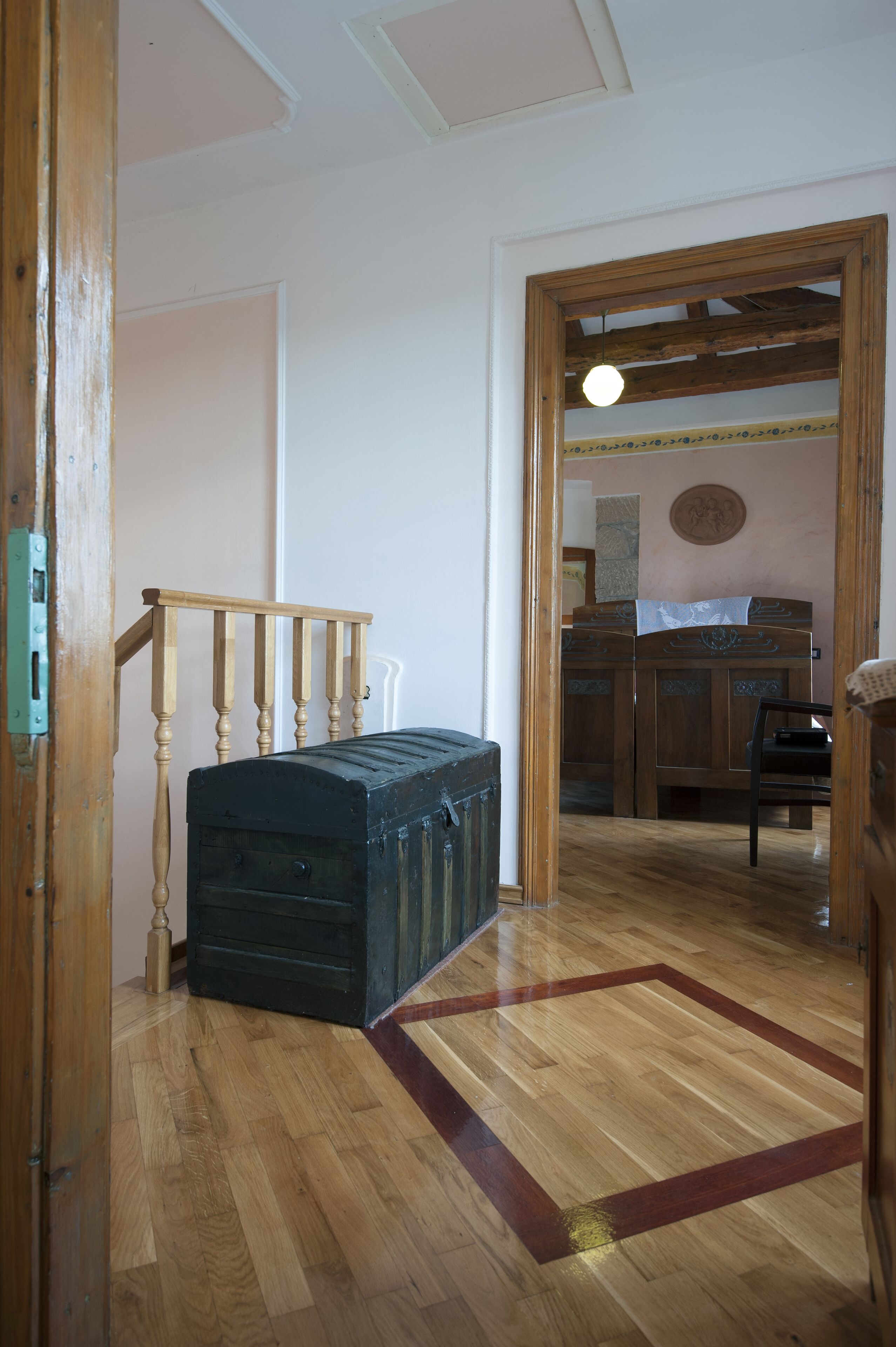 A room with a wooden staircase, a large black trunk, and a wooden cabinet in the background.