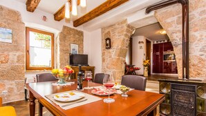 A dining area with a wooden table set for four, a stone wall, a fireplace, and a television in the background. - House Kras (Kras)