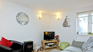 A living room with a sofa, a black leather chair, a TV, a wooden side table, and a decorative mirror on the wall.
