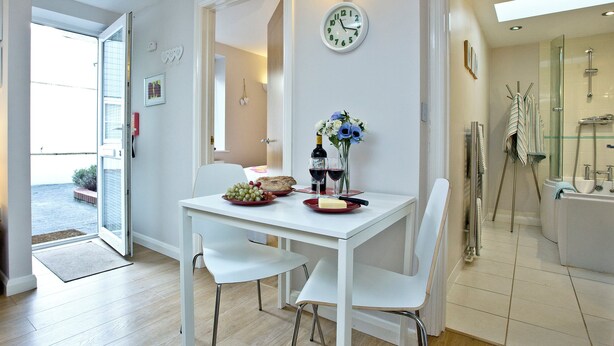 A modern dining area with a white table, chairs, and a wall clock.