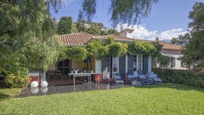A house with a tiled roof, a patio with outdoor furniture, and a well-maintained lawn. - Villa Wisteria (Funchal)