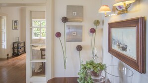 A hallway with a wooden floor, a dining area with a table and chairs, and a wall with framed artwork and wall-mounted lamps. - Villa Wisteria (Funchal)