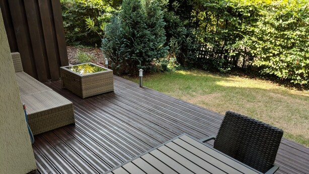 Eine Holzterrasse mit Gartenmöbeln, darunter ein Tisch und zwei Stühle.