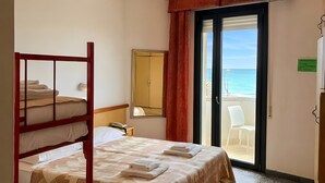 Une chambre d’hôtel avec un lit superposé, un lit simple, une grande fenêtre donnant sur la mer, une porte menant à un balcon et un luminaire au plafond.
