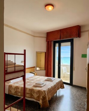 Habitación de hotel con literas, una cama individual, un ventanal con vistas al mar, una puerta que da a un balcón y una lámpara en el techo.