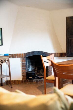 A room with a fireplace, a wooden table, and a chair. - MASOVERS A, 3 bedrooms, 1–6 people (max. 8—2 on a sofa bed), 5 min. from the beach (Castelló d'Empúries)