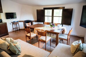 A dining area with a wooden table, chairs, and a television on the wall. - MASOVERS A, 3 bedrooms, 1–6 people (max. 8—2 on a sofa bed), 5 min. from the beach (Castelló d'Empúries)