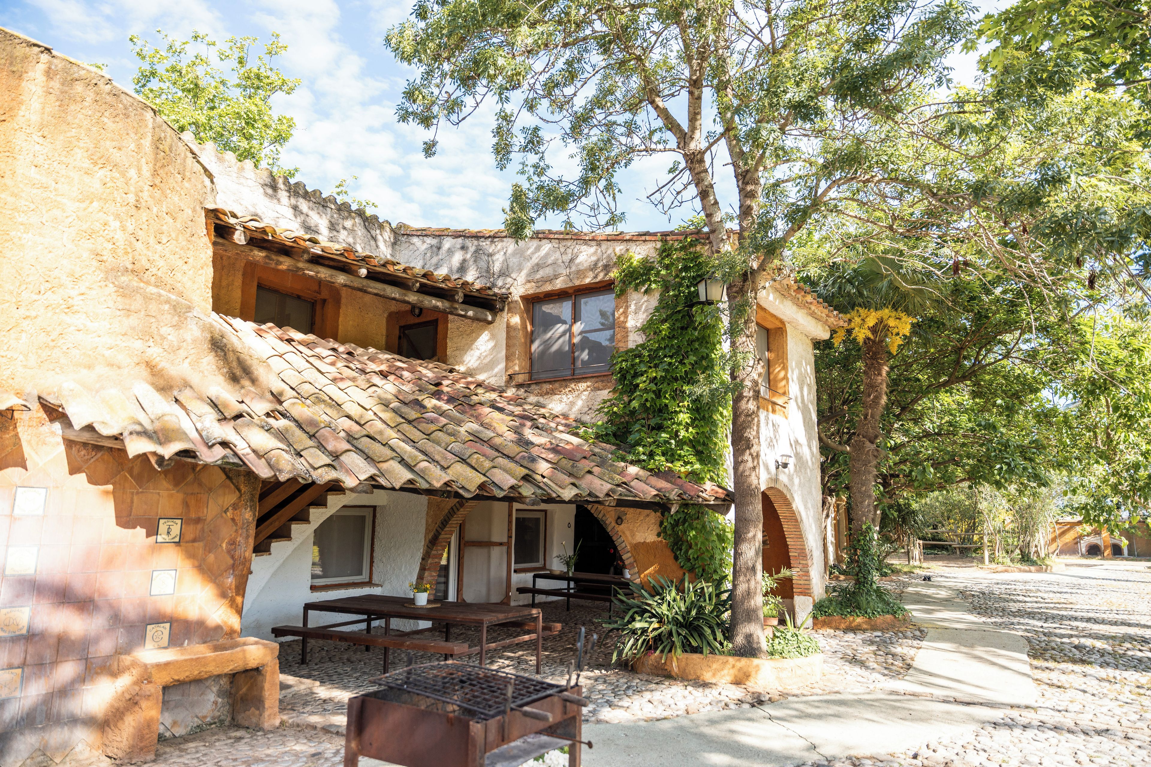 A rustic building with a tiled roof, a covered patio, and a stone wall.