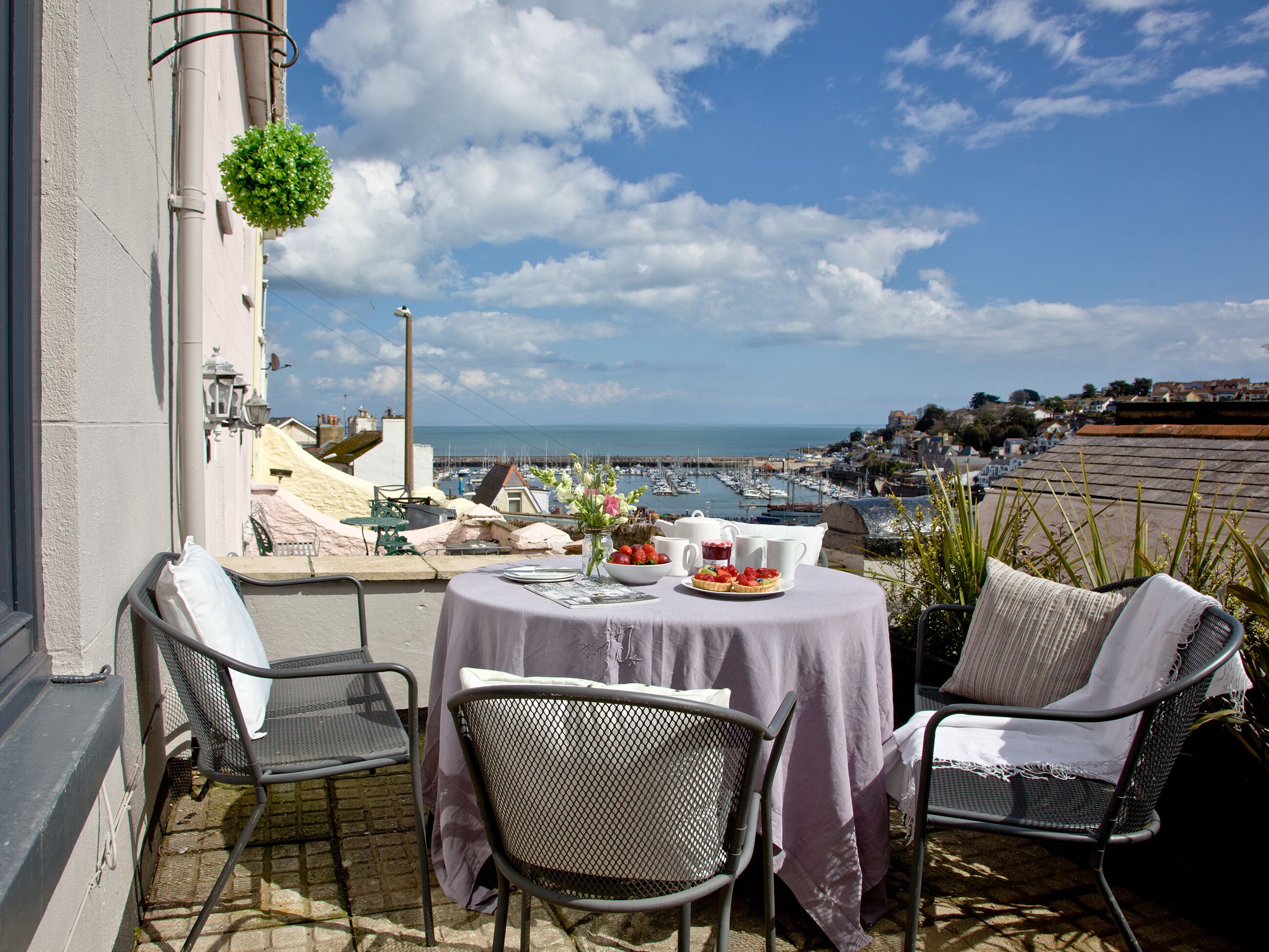 Une terrasse avec une table dressée pour deux personnes, offrant une vue sur un port de plaisance et une ville côtière.