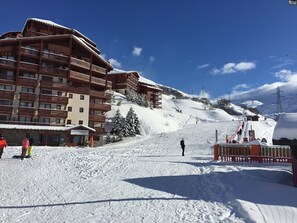A multi-story wooden building with balconies, likely a hotel, set against a snowy mountain backdrop.