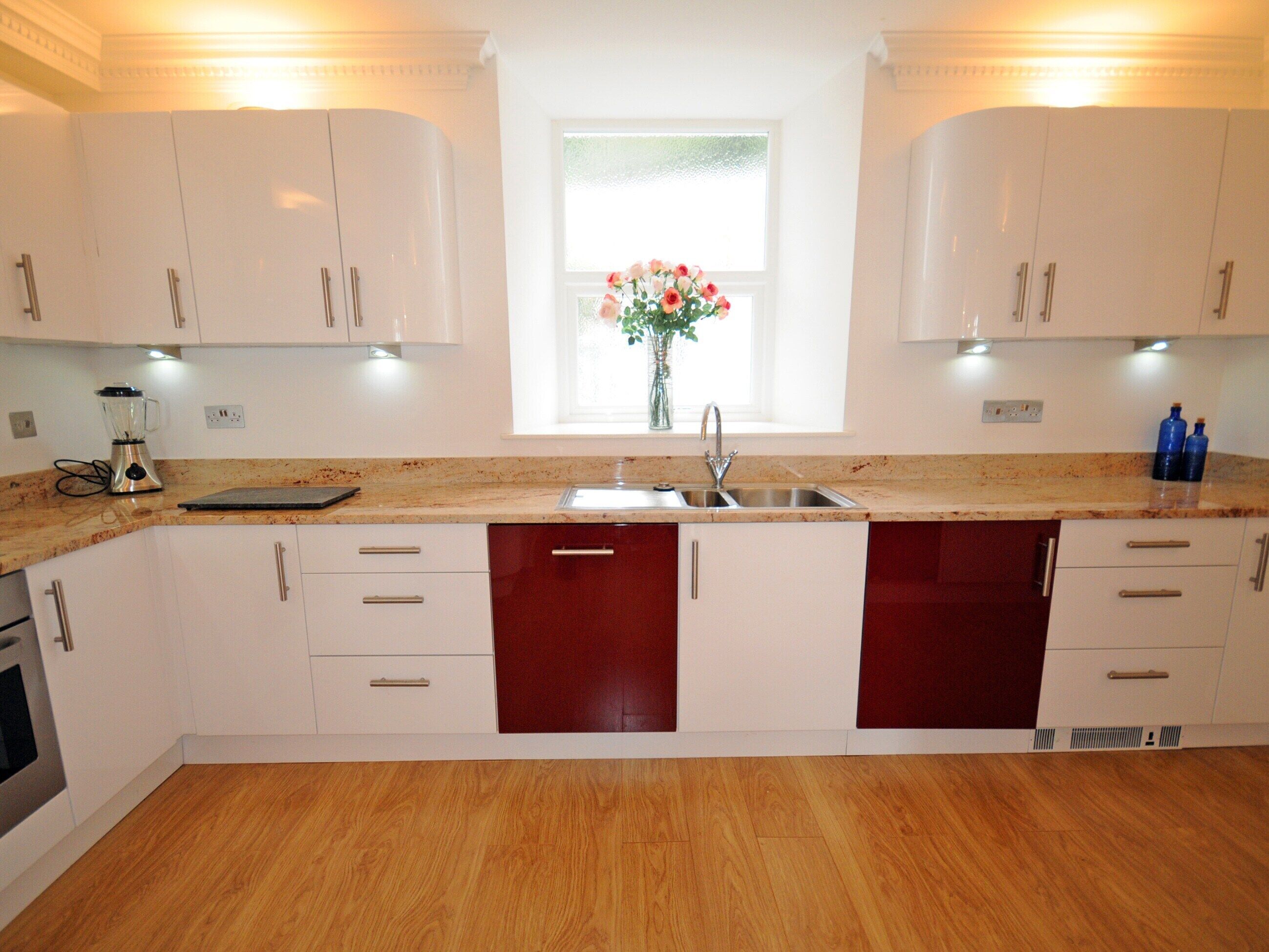 A modern kitchen with white cabinets, a wooden countertop, a built-in dishwasher, and a window with a flower vase.