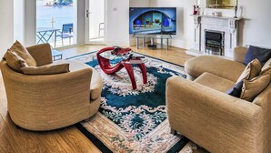 Ein geräumiges Wohnzimmer mit großem Fernseher, bequemen Sitzgelegenheiten, einem Kamin und Meerblick.