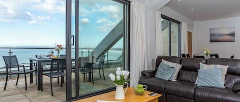 A modern living room with a large sliding glass door leading to a balcony overlooking the sea.