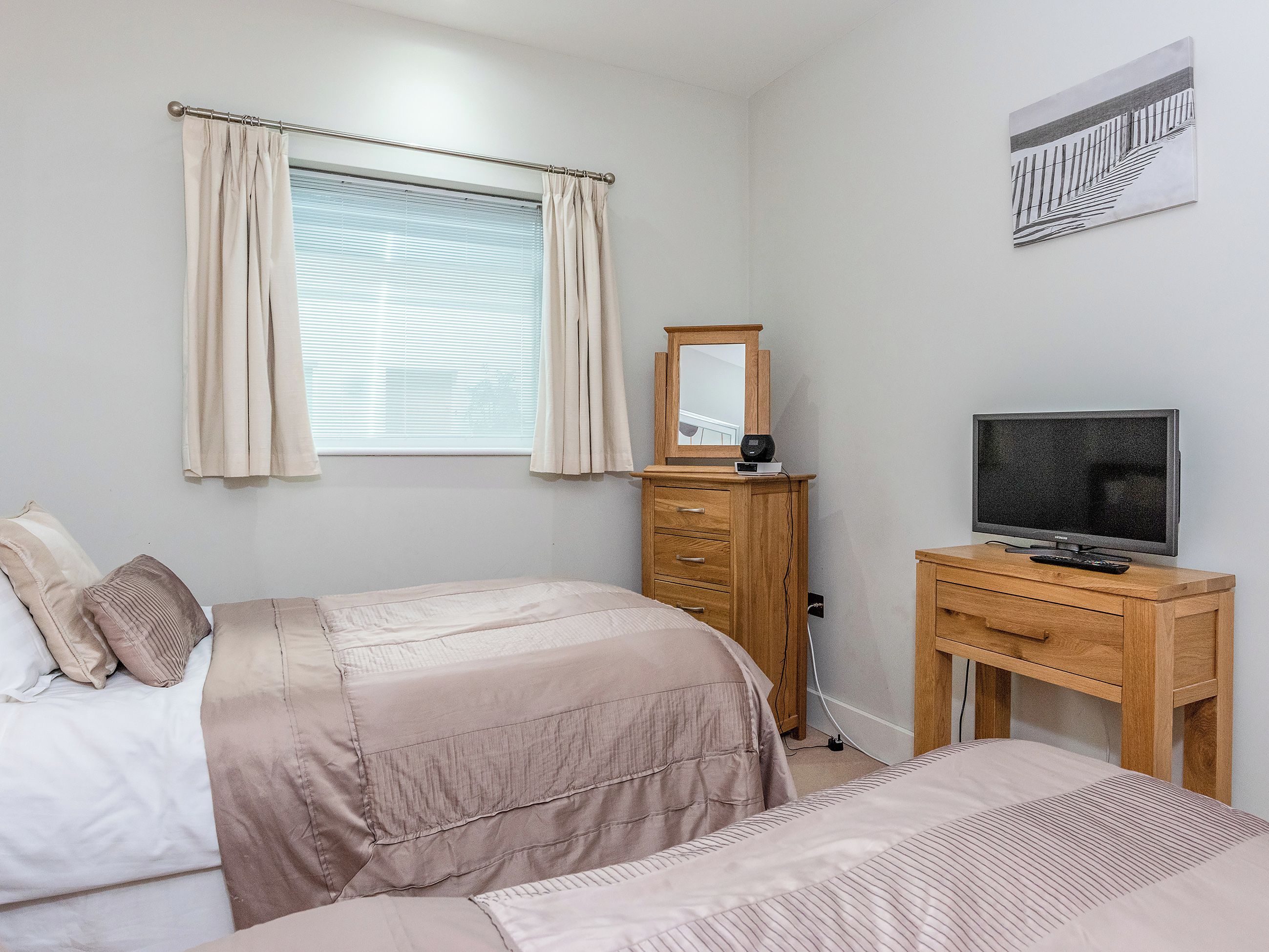 Een slaapkamer met een bed, een dressoir, een televisie en een raam met gordijnen.
