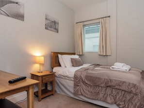 A bedroom with a bed, bedside table, lamp, and a window with curtains. - 3 bedroom accommodation in Westward Ho! (Westward Ho!)