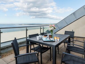 A table with breakfast items, a vase of flowers, and a view of the beach. - 3 bedroom accommodation in Westward Ho! (Westward Ho!)