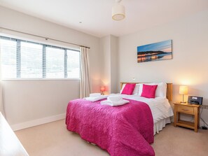 A hotel room with a bed, a nightstand, a lamp, a painting, and a window with curtains. - 3 bedroom accommodation in Westward Ho! (Westward Ho!)