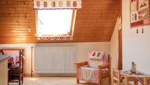 A cozy room with a wooden ceiling, a window with a checkered curtain, a radiator, a wooden chair, a small table with a bottle, and a wall with a checkered pattern. - Homerez - House in Triembach-au-Val (Triembach-au-Val)