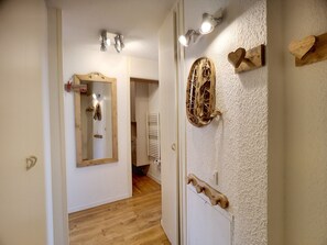 Un pasillo con una puerta de madera, un espejo y una lámpara fijada a la pared.