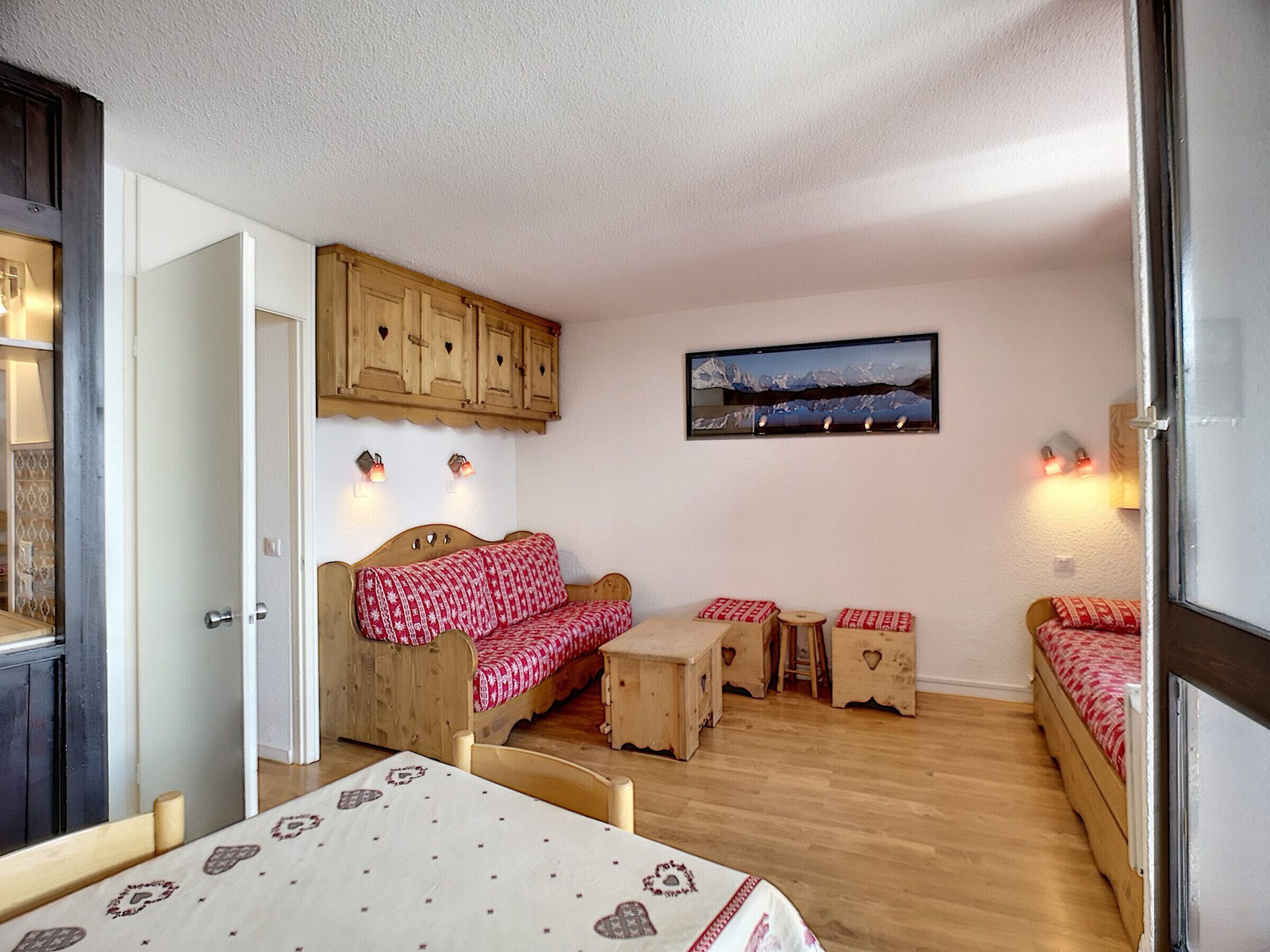 Quarto aconchegante com cama de madeira, uma mesinha e uma cadeira. Há um armário de madeira acima da cama e um quadro na parede.