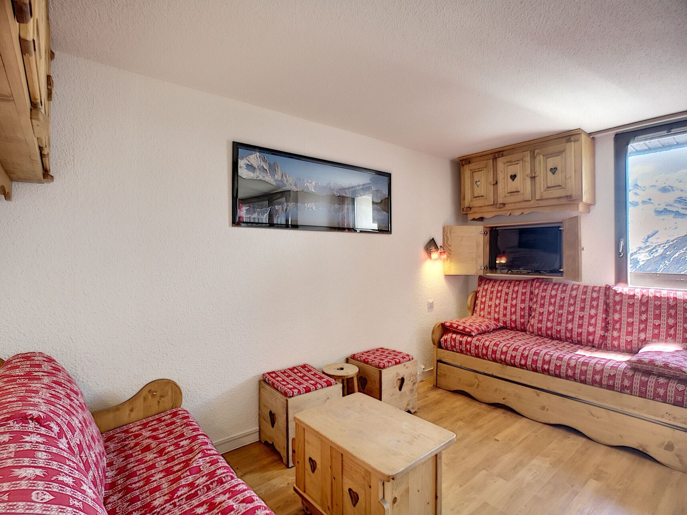 Ein gemütliches Blockhaus-Interieur mit einer Holzcouch, einem kleinen Holztisch und einem aufgehängten Bild von einem verschneiten Berg.